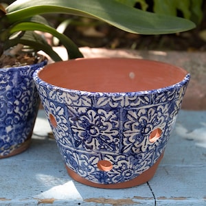 May include: Blue and white ceramic planter with a terracotta rim and drainage holes. The planter has a floral pattern.