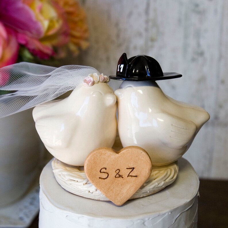 K&ouml;nnte beinhalten: Ein wei&szlig;er Keramik-Vogel-Kuchentopper f&uuml;r Hochzeiten mit einem schwarzen Feuerwehrhut, einem Schleier und einer herzf&ouml;rmigen Plakette mit der Aufschrift "S&Z".