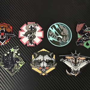 May include: A collection of seven tactical morale patches featuring various graphic designs including a roaring bear with a rifle, a medical snake symbol, a wolf, a bird of prey with a sniper rifle, a crow, a raccoon with tools, and a flying squirrel.