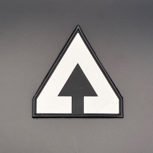 Könnte beinhalten: Ein schwarz-weißes Abzeichen mit einem weißen Dreieck und einem schwarzen Pfeil, der nach oben zeigt. Das Abzeichen hat einen schwarzen Rand und ist vor einem grauen Hintergrund platziert.