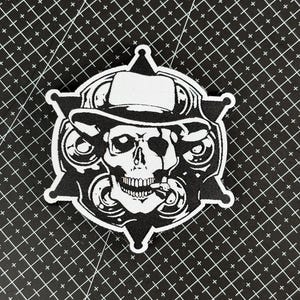 May include: A black and white patch featuring a skull wearing a hat and a badge. The skull has a cigarette in its mouth and is surrounded by a star-shaped border. The patch is likely for clothing or accessories.