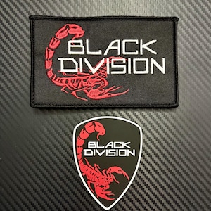 Puede incluir: Un parche rectangular negro bordado y un parche negro en forma de escudo, ambos con un gráfico de escorpión rojo y el texto blanco "BLACK DIVISION". El parche rectangular tiene un borde cosido, mientras que el parche de escudo tiene un contorno blanco.