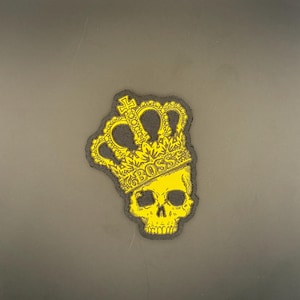 Op de afbeelding: Gele schedelpatch met een kroon en het woord "BOSS". De patch heeft een zwarte rand op een grijze achtergrond. De schedel heeft oogkassen en een neusholte. De kroon heeft een kruis erop.