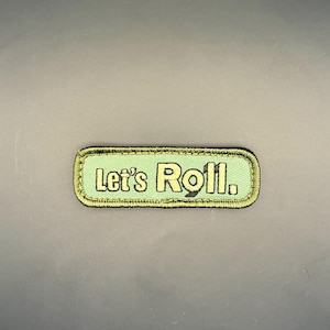 May include: A rectangular embroidered patch with a light green background and a dark green border. The text Let's Roll. is stitched in a dark green font across the center of the patch. The patch features a clean, stitched edge finish.