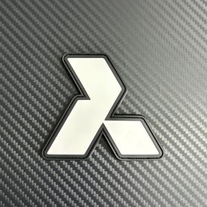 Op de afbeelding: Een wit en zwart embleem met een gestileerd geometrisch ontwerp. Het embleem heeft een witte binnenkant en een zwarte rand. De achtergrond is een donkergrijze, getextureerde ondergrond.