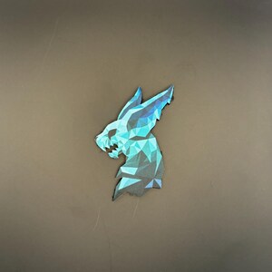 May include: A geometric design of a creature's head, featuring shades of blue and teal. The design is made up of triangular shapes, giving it a modern, low-poly appearance. The creature's head is facing to the left.