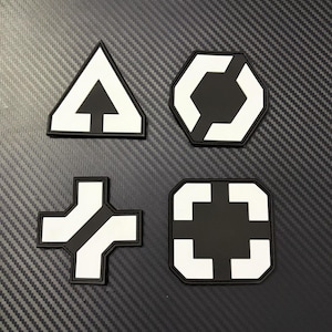 May include: Four black and white geometric patches. The shapes include a triangle with an arrow, a hexagon with a cutout, a cross with a diagonal line, and a square with inward-facing corners.