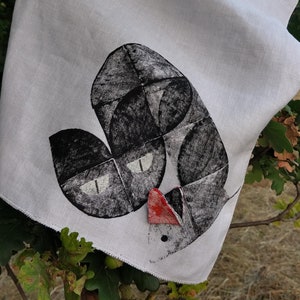 Könnte beinhalten: Ein weißes Leinen-Geschirrtuch mit einer schwarz-weißen Illustration einer Katze mit roter Nase. Die Katze ist in geometrischem Stil gedruckt.
