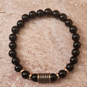 May include: Black beaded bracelet with a silver metal accent. The bracelet is made of round black beads and a silver metal spacer bead.