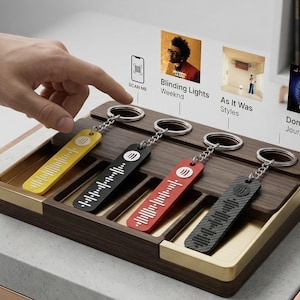 以下が含まれることがあります： 木製の音楽をテーマにしたキーホルダーホルダー。黄色、黒、赤、グレーの4つのキーホルダーが付いています。各キーホルダーには、ユニークなオーディオ波形デザインがあります。ホルダーは金色のトリムで、「SCAN ME」と書かれたQRコードが付いています。