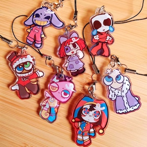 May include: Seven colourful acrylic charms depicting cartoon characters, each with a unique design. They are attached to black lanyards. The characters display diverse outfits and expressions, using vibrant colours such as red, purple, and blue.