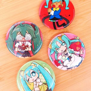 Op de afbeelding: Vier ronde pins met illustraties in anime-stijl. De pins tonen kleurrijke ontwerpen van een personage met lang turquoise haar, in verschillende poses en outfits, tegen rode, roze en groene achtergronden.