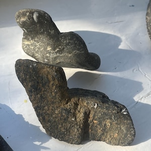 May include: Two dark gray, rough, natural stone sculptures. The sculptures are abstract and resemble animal forms. The sculptures are on a white surface.