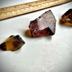 May include: Three pieces of amber, one is a deep red color, one is a light amber color, and the other is a dark amber color.