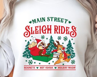 May include: White sweatshirt with a Christmas-themed design featuring Chip and Dale riding a sleigh. The text reads "Main Street Sleigh Rides" with the words "beignets, hot cocoa, holiday magic" below the image.