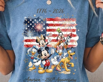 May include: Blue t-shirt featuring a graphic of the American flag with fireworks and Disney characters. The shirt has the text "1776-2026" and "America - 250th Anniversary" in a script font.