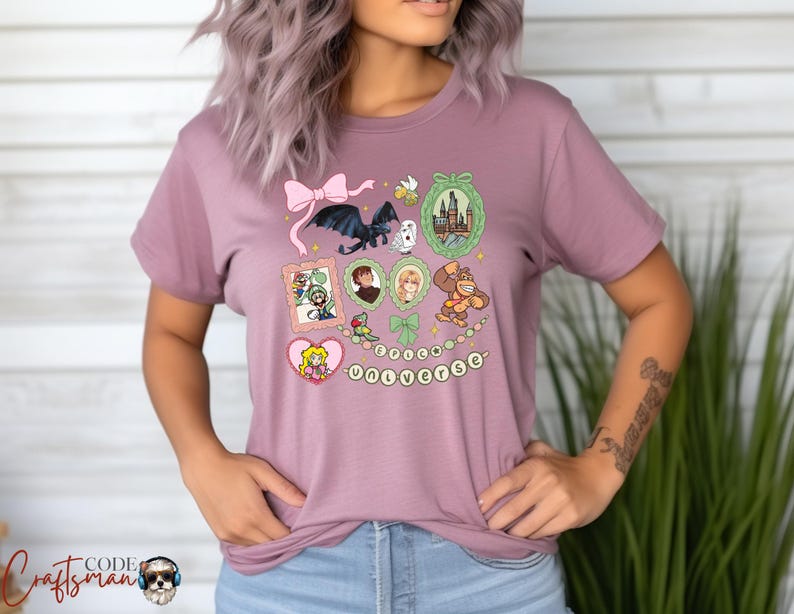 May include: Mauve t-shirt featuring a collection of cartoon illustrations, including a dragon, castle, and characters from various franchises. The word "UNIVERSE" is spelled out in a string of beads. A pink bow is at the top.