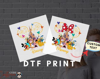 May include: Two white t-shirts with a Disney theme. The left shirt has a castle and Mickey Mouse characters with the text "Daddy". The right shirt has a castle and Mickey Mouse characters with a red bow and the text "Mommy".