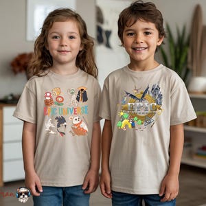 May include: Two children wearing beige t-shirts. The shirt on the left has the text "The Universe" with cartoon graphics. The shirt on the right has the word "EPIC" with cartoon graphics. Both shirts have short sleeves.