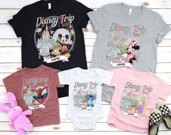 May include: A collection of Disney Trip 2026 t-shirts and a onesie in various colors, including black, gray, maroon, white, and pink. Each shirt features a different Disney character and the text "Disney Trip 2026" with a space for a name.