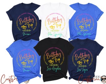 May include: A collection of short-sleeved t-shirts in various colors, including navy, white, and black. Each shirt features a circular design with the words "Birthday Trip 2026" and a destination city, such as Miami or Las Vegas.