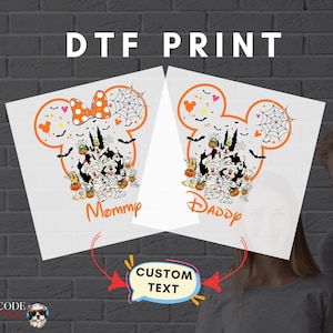 Peut inclure: Deux impressions DTF blanches avec un motif Mickey Mouse sur le thème d'Halloween. L'une dit "Mommy" et l'autre "Daddy". Le motif comprend des chauves-souris, des citrouilles et une toile d'araignée.
