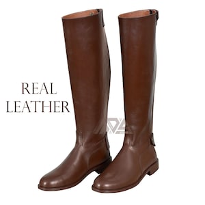 Puede incluir: Un par de botas de montar de cuero marrón con una cremallera en la parte posterior de cada bota. Las botas son altas y tienen una punta puntiaguda. El texto "REAL LEATHER" está impreso en la imagen.