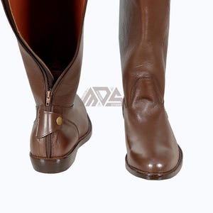 May include: A pair of brown leather riding boots with a zipper on the inside of the boot. The boots have a pointed toe and a low heel.