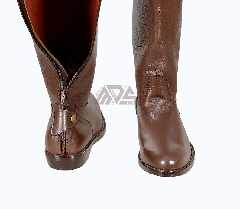 May include: A pair of brown leather riding boots with a zipper on the inside of the boot. The boots have a pointed toe and a low heel.