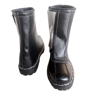 May include: A pair of black leather boots with a white panel on the side. The boots have a zipper on the inside of the ankle and a white stitch detail around the sole.