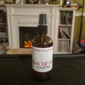 Può includere: Una bottiglia di vetro marrone con un ugello spray nero e un'etichetta bianca che recita "Naughty Faery Creations Back Off B*tch A Divine Mystical Blend Crafted in Port Ludlow, WA".