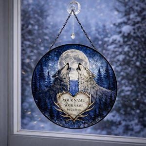 Könnte beinhalten: Runde Glasmalerei mit zwei Wölfen, die einen Vollmond in einem sternenklaren Nachthimmel anheulen. Ein herzförmiges Emblem unten enthält den Text "YOUR NAME + YOUR NAME 01/23/2010". Das Kunstwerk wird von einer Kette gehalten.