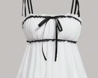 May include: White camisole with black trim and straps. The top features a ruffled neckline and a bow detail at the center. The straps are adjustable and tie at the shoulders. The fabric appears lightweight and flowy.