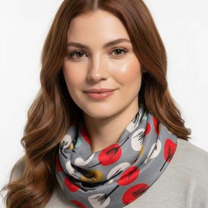 May include: A grey infinity scarf featuring a pattern of red, white, and yellow circular shapes with black stems. The scarf is made of a soft material and is worn around the neck.