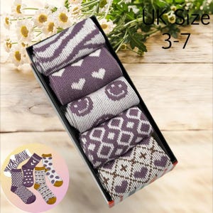 May include: A box of six pairs of women's socks. The socks are in various patterns, including stripes, hearts, and smiley faces. The socks are purple, white, and brown. The box says "UK Size 3-7".