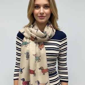 May include: A beige scarf with a repeating pattern of dachshunds in different outfits. The scarf is draped around the neck. The background is a striped top and skirt.