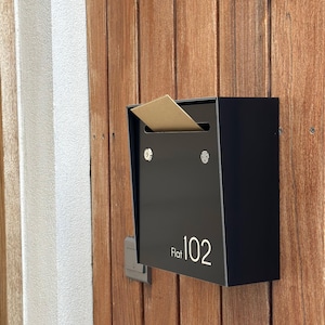 May include: Black mailbox with a brown envelope sticking out of the slot. The mailbox has a white label that says "Flat 102".