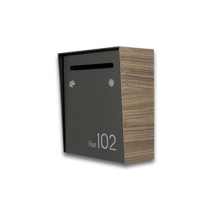 May include: A modern mailbox with a dark gray front and a wood-grain side. The mailbox has a slot for mail and the number "102" is printed on the front. The mailbox is designed to be mounted on a wall.