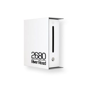 May include: A modern white mailbox with a black accent design. The mailbox features the address "2680 River Road" in black lettering. It has a vertical black slot and a small keyhole.