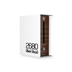 May include: A modern mailbox with a white front and a wood-grain side panel. The mailbox features the address "2680 River Road" in black lettering. It has a slot for mail and a small lock.