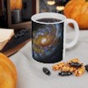 May include: White ceramic coffee mug with a colorful galaxy print. The galaxy print features a swirling nebula with a bright star in the center.