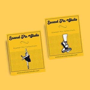 Può includere: Due design di spille smaltate che raffigurano una ballerina e una scarpa da ballet. La spilla della ballerina è in bianco e nero e la spilla della scarpa da ballet è nera con uno striscione bianco che dice "DANCER". Entrambe le spille sono su uno sfondo giallo con un motivo a griglia e il testo "Enamel Pin Studio" e "Enamel Pin Collections".