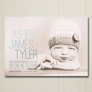 May include: A newborn baby boy named Asher James Tyler, wearing a knitted hat with a button, is pictured on a light brown background. The baby is 6 pounds, 5 ounces and 21 inches long. The text "Welcomed with love on 10.09.15" is printed below the baby's picture. The text "proud parents, LUKE AND SARA" is printed below the date.