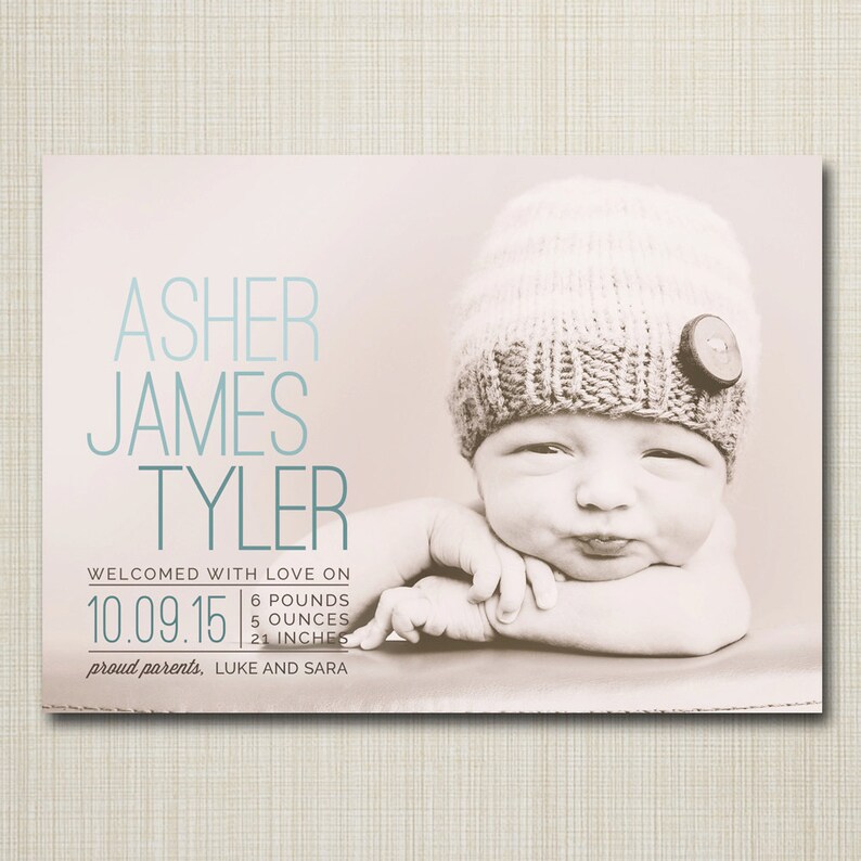 May include: A newborn baby boy named Asher James Tyler, wearing a knitted hat with a button, is pictured on a light brown background. The baby is 6 pounds, 5 ounces and 21 inches long. The text "Welcomed with love on 10.09.15" is printed below the baby's picture. The text "proud parents, LUKE AND SARA" is printed below the date.