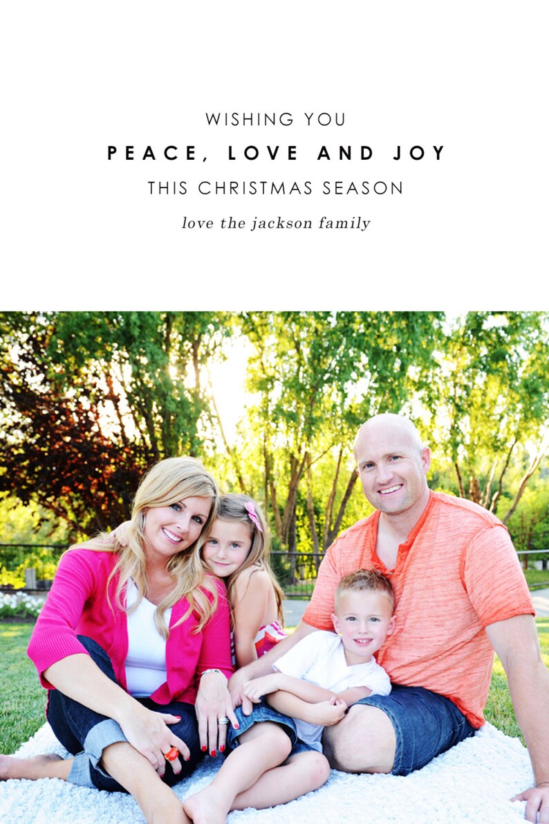 May include: A family of four, a mum, dad, and two children, are sitting on a white blanket in a grassy park. The parents are wearing casual clothing, while the children are wearing colourful shirts. The family are smiling and looking at the camera. The text "Wishing you peace, love and joy this Christmas season love the Jackson family" is displayed above the image.