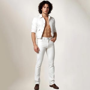 May include: A man wearing a white denim jacket and white jeans. He is standing with his hands in his pockets and looking at the camera.
