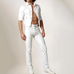May include: A white leather jacket with a zipper closure and a white button-down shirt underneath. The person is wearing white jeans with a thin black belt.