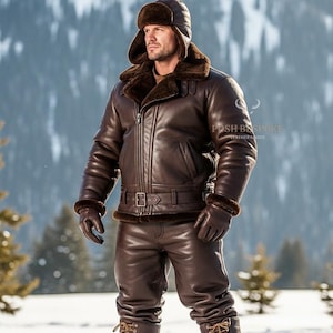 Könnte beinhalten: Braune Lederjacke, Hose, Handschuhe und Hut mit Fellbesatz. Die Jacke hat einen Reißverschluss und einen Gürtel. Das Outfit wird in einer schneebedeckten, bergigen Umgebung getragen. Das Gesamtthema ist Winterbekleidung.