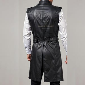 Op de afbeelding: Zwart leren vest met een lange lijn, met een ceintuur in de taille en schouderaccenten. Het vest wordt gedragen over een wit overhemd met knopen. De achterkant van het vest heeft de tekst "POSH BESPOKE LEATHER GOODS".