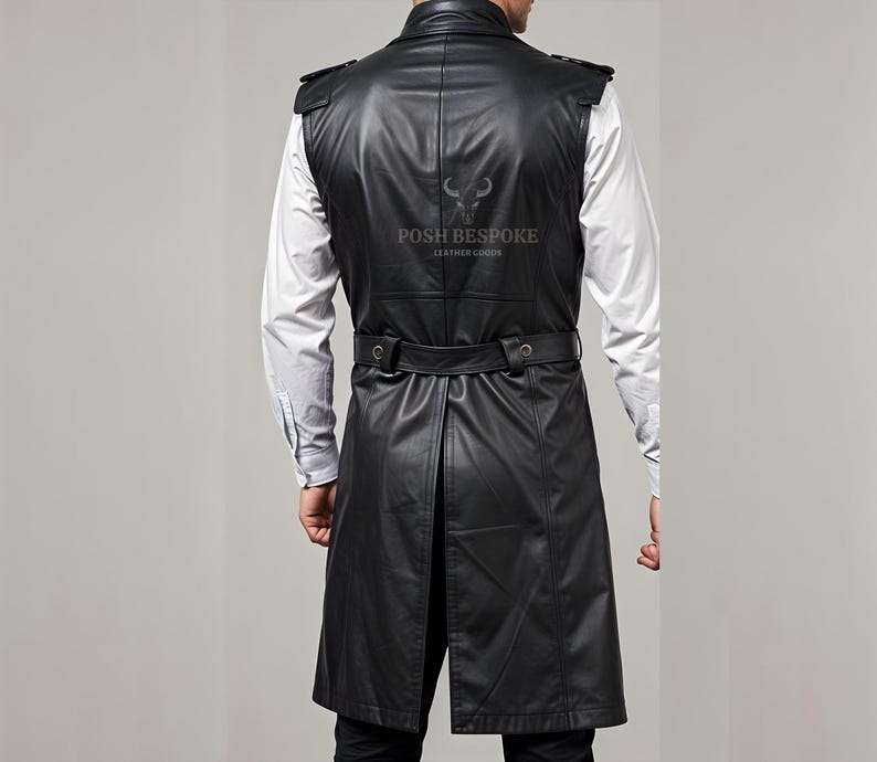 Op de afbeelding: Zwart leren vest met een lange lijn, met een ceintuur in de taille en schouderaccenten. Het vest wordt gedragen over een wit overhemd met knopen. De achterkant van het vest heeft de tekst "POSH BESPOKE LEATHER GOODS".